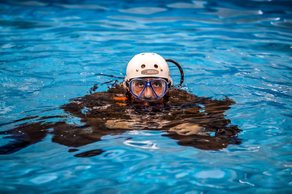 Diving offshore survival instructor in a pool with trainees delivering advice on sea survival.