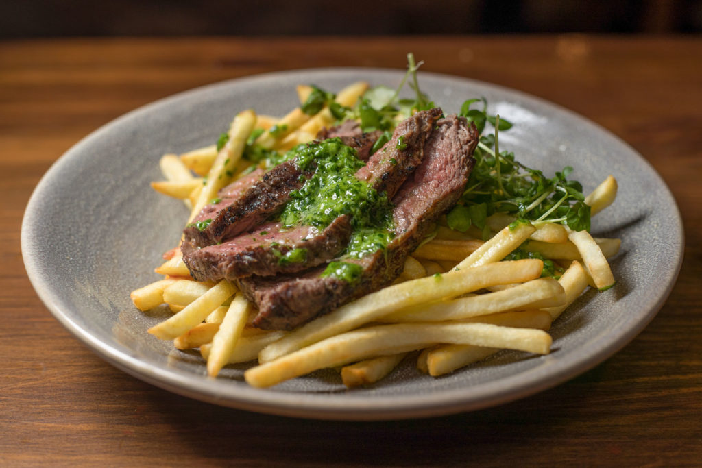 Food Photography Aberdeen by Scott Cameron Baxter. Picture shows three cut steak strips with fries and green garlic sauce poured over the strips on a plate photographed top down.