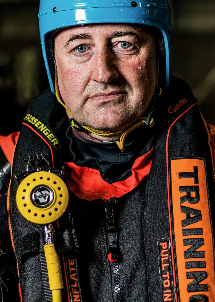 Man in offshore survival suit, with a CA-EBS breathing system lifejacket after being in the water. Blue helmet. Picture is taken in portrait with dramatic lighting from the left. Photo by Scott Cameron Baxter Aberdeen, PR, Commercial and Product photographer.