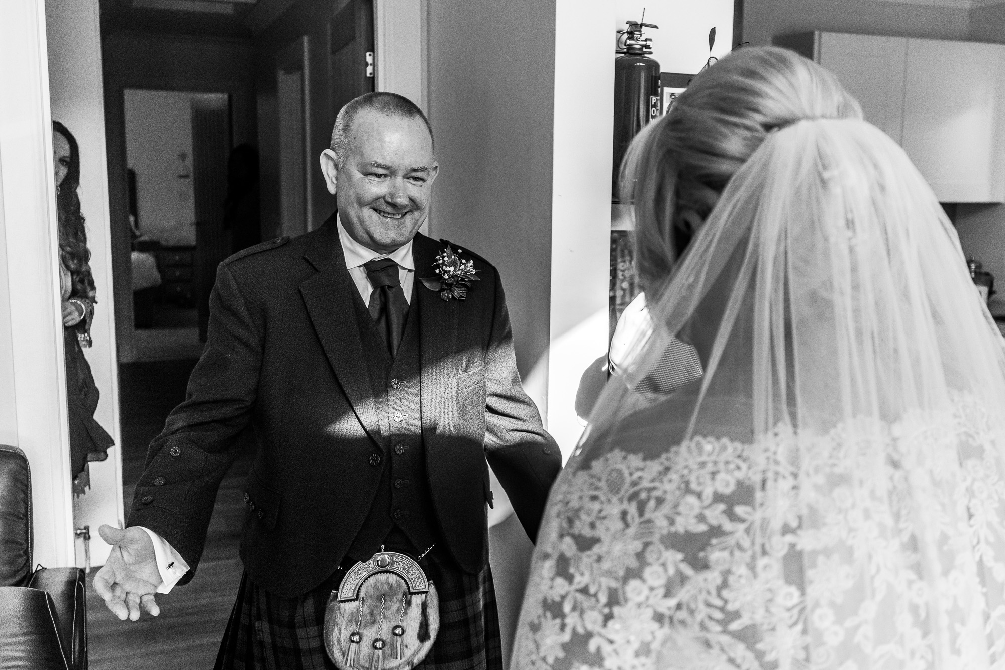 A black and white image of a father seeing his daugher for the first time in her wedding dress. The First look. Image captured from behind the brides shoulder who is on the right of the image, the father in the centre. Wedding photographer Aberdeen, Picture by Scott Cameron Baxter.