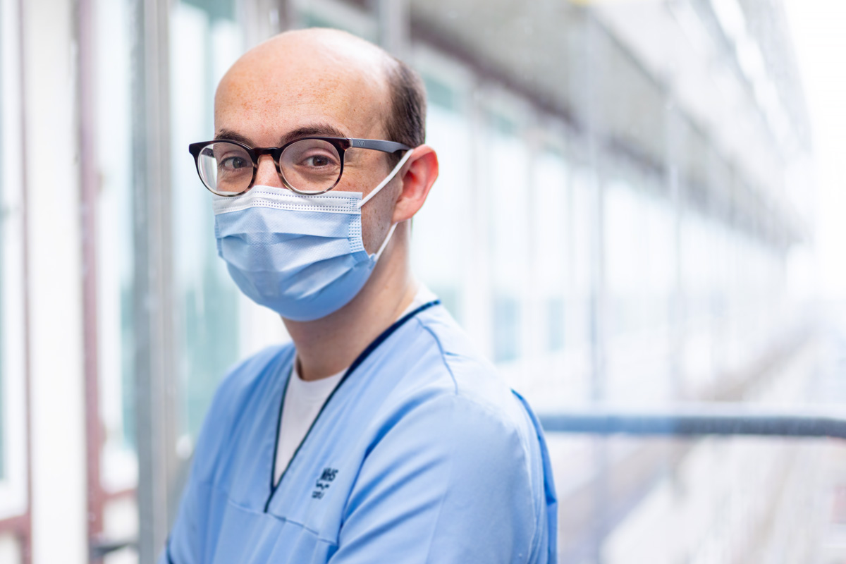 Press photographer aberdeen Scott Cameron Baxter, image shows a nurse in Aberdeen Royal Infirmary, wearing blue scrubs and a blue face mask. He has glasses, the background is blurred with his face only in focus. The background is a view from a window on a bright day. Photographs by Aberdeen press and commercial photographer Scott Cameron Baxter.