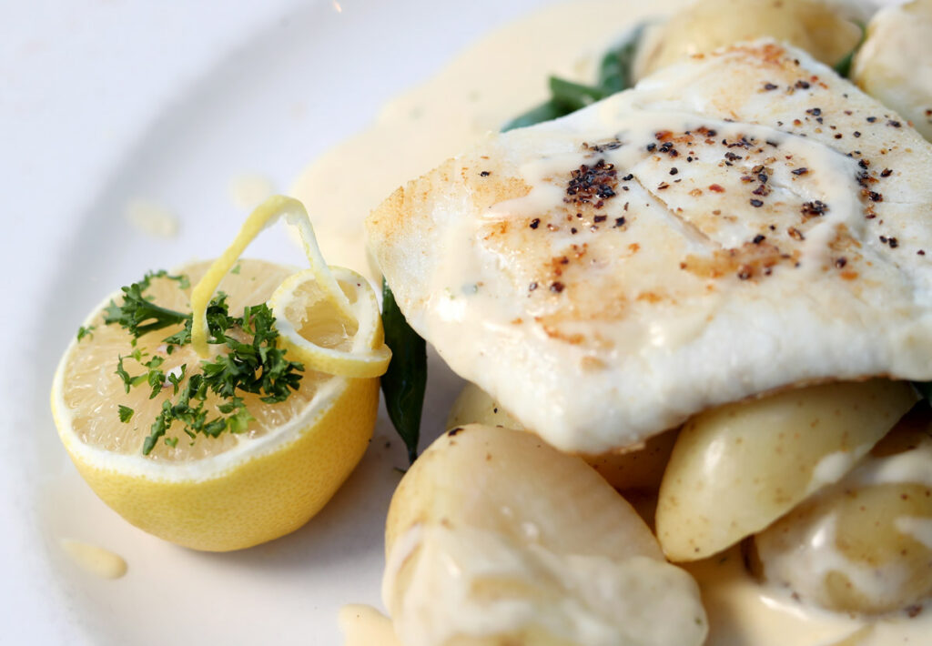 Aberdeen Food and drink photographer Scott Cameron Baxter. Picture shows a close up image of a plate of white fish on the right with a lemon on the left, the light is bright and lighting the whiter plate and food well.
