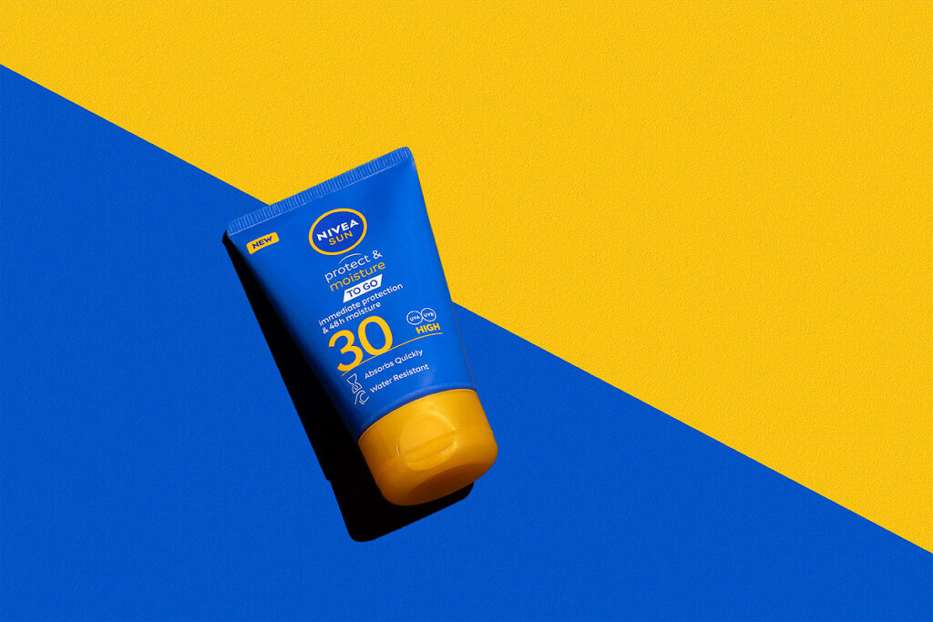 Commercial Scotland Product Photographer Aberdeen - Scott Cameron Baxter. Image shows a a suncream bottle, which is blue with a mustard colour cap. It is on a two tone colour surface, Blue and mustard colour, which is cut off diagonally to match the bottles colours. There is a razor edge shadow to the left leaving a silhouette of the bottle.