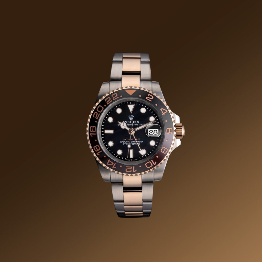 A picture of a Rolex GMT Master 2. Photographed by commercial product photographer Scott Cameron Baxter from Aberdeen, Scotland. The watch is suspended in air, facing forward straight on. The background is a gradient golden brown, The watch is set to 10:12. The Rolex has a silver clasp with gold inlay, brown and black bezel. 