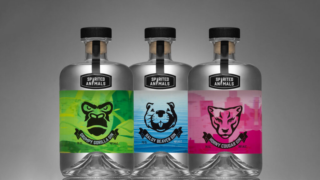 Three bottles of gin by Spirited Animals are in a line. One with a green label, blue lable and pink label. The background is grey contrasting against the bottles, the image is in a widescreen format.